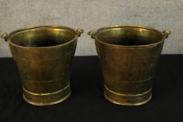 A pair of early 20th century brass buckets, each with swing handles and raised on circular foot.