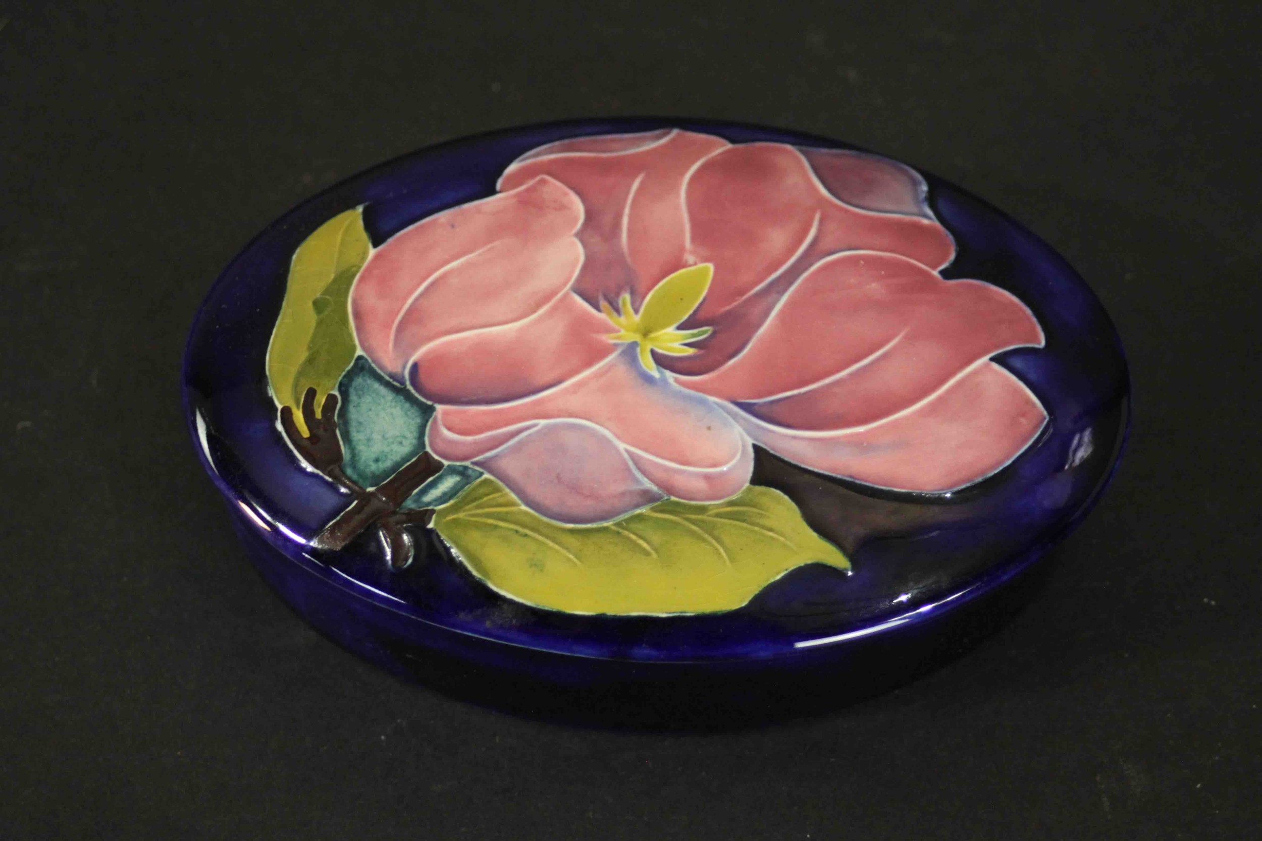 A Moorcroft pink magnolia on blue ground oval powder box. Maker's mark to the base. H.3 W.13cm.