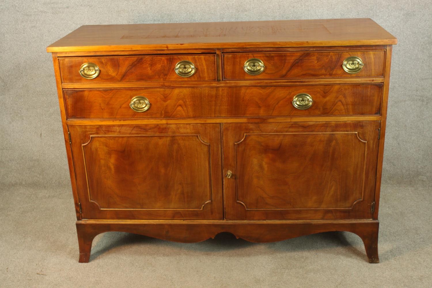 A Georgian style two short over one long drawer with twin cabinet doors below raised on shaped