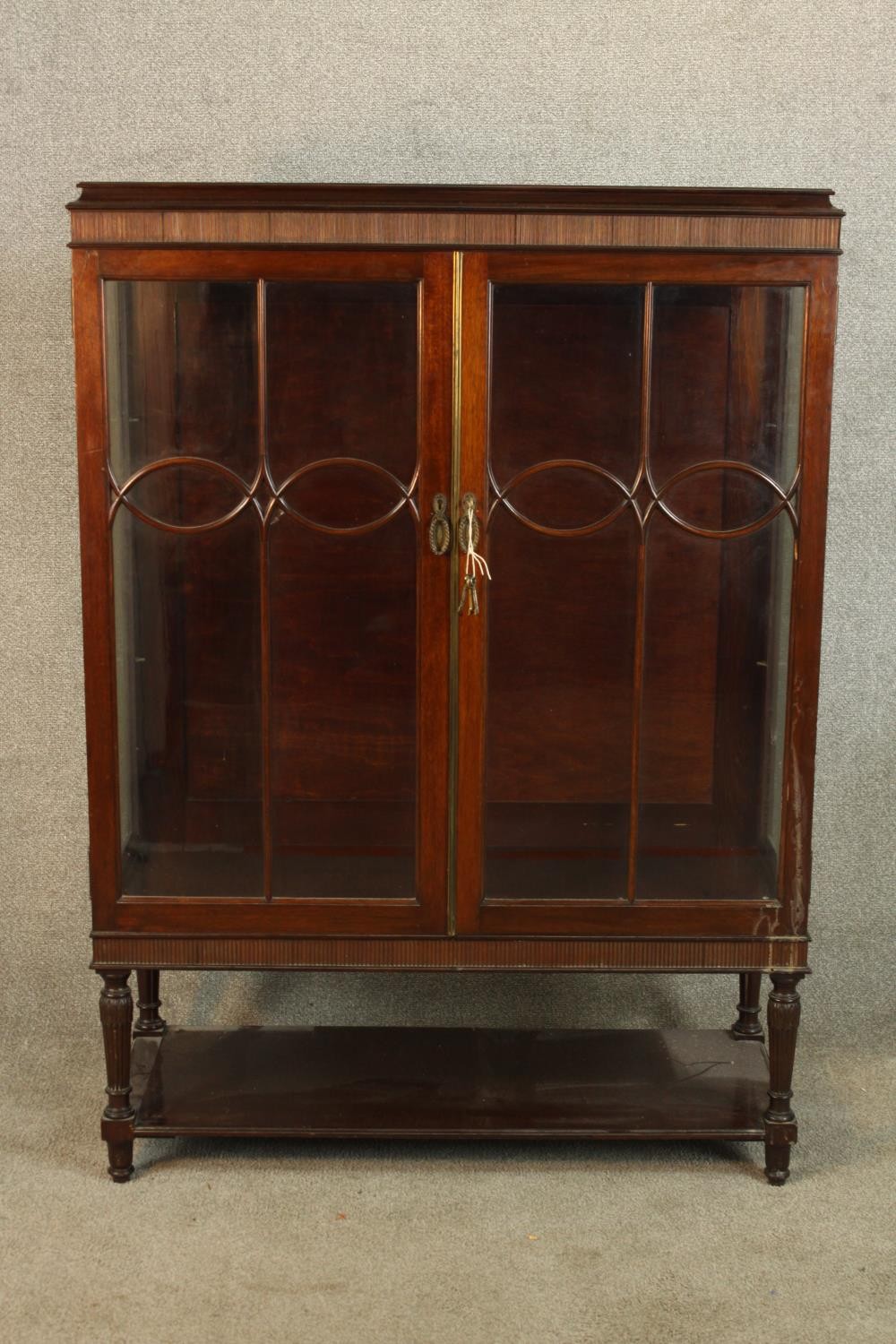 A late 19th/early 20th mahogany twin door display cabinet raised on turned supports and shelf