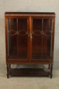 A late 19th/early 20th mahogany twin door display cabinet raised on turned supports and shelf
