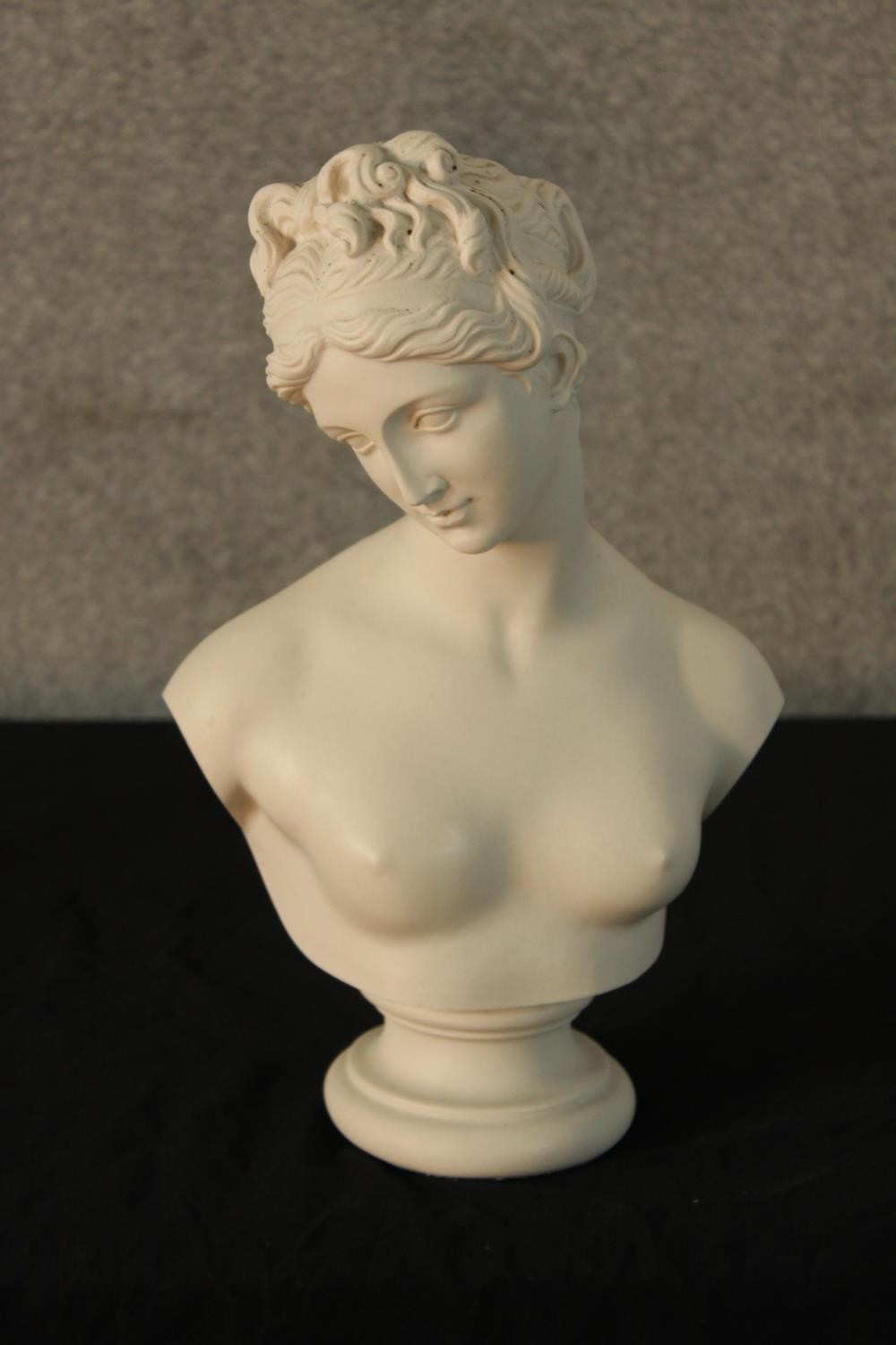 An early 20th century painted porcelain bust of a semi clad classical lady raised on turned socle