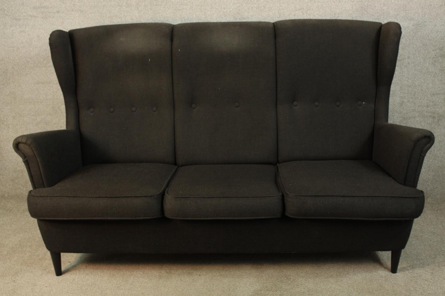 A contemporary black upholstered three person button back and scroll arm sofa raised on tapering