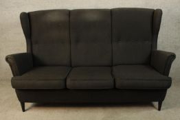 A contemporary black upholstered three person button back and scroll arm sofa raised on tapering