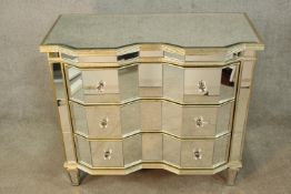 A contemporary inverted breakfront mirrored three long drawer chest of drawers raised on tapering