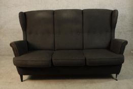 A contemporary black upholstered button back three seater scroll arm sofa raised on tapering