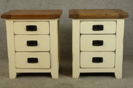 A pair of painted oak three drawer bedside chest of drawers with iron swing handles raised on shaped