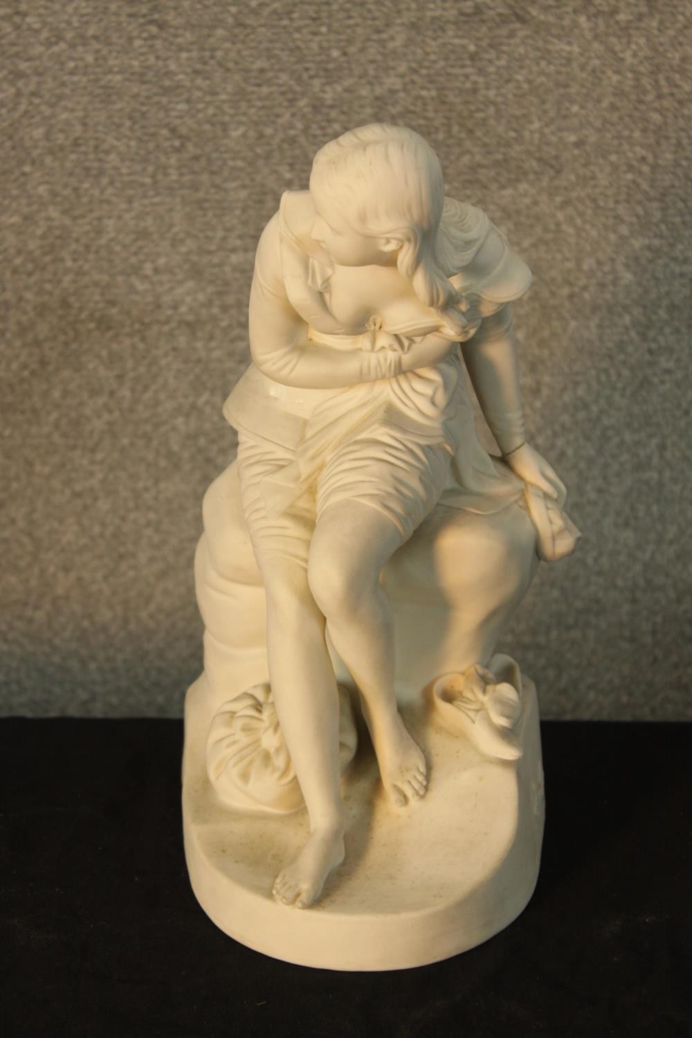 A 19th/early 20th century Parianware figure of a lady sitting on a rock with a sack at her feet,