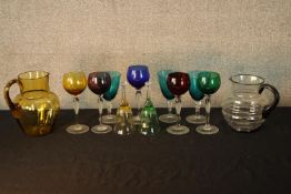 Assorted vintage coloured drinking glasses together glass bells and two glass lemonade jugs. H.19cm.