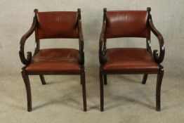 A pair of Regency style mahogany framed and red leather open arm chairs raised on sabre supports.