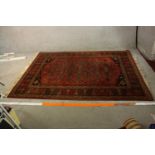 A late 19th century Persian woollen rug with stylised geometric motifs on a burgundy field within