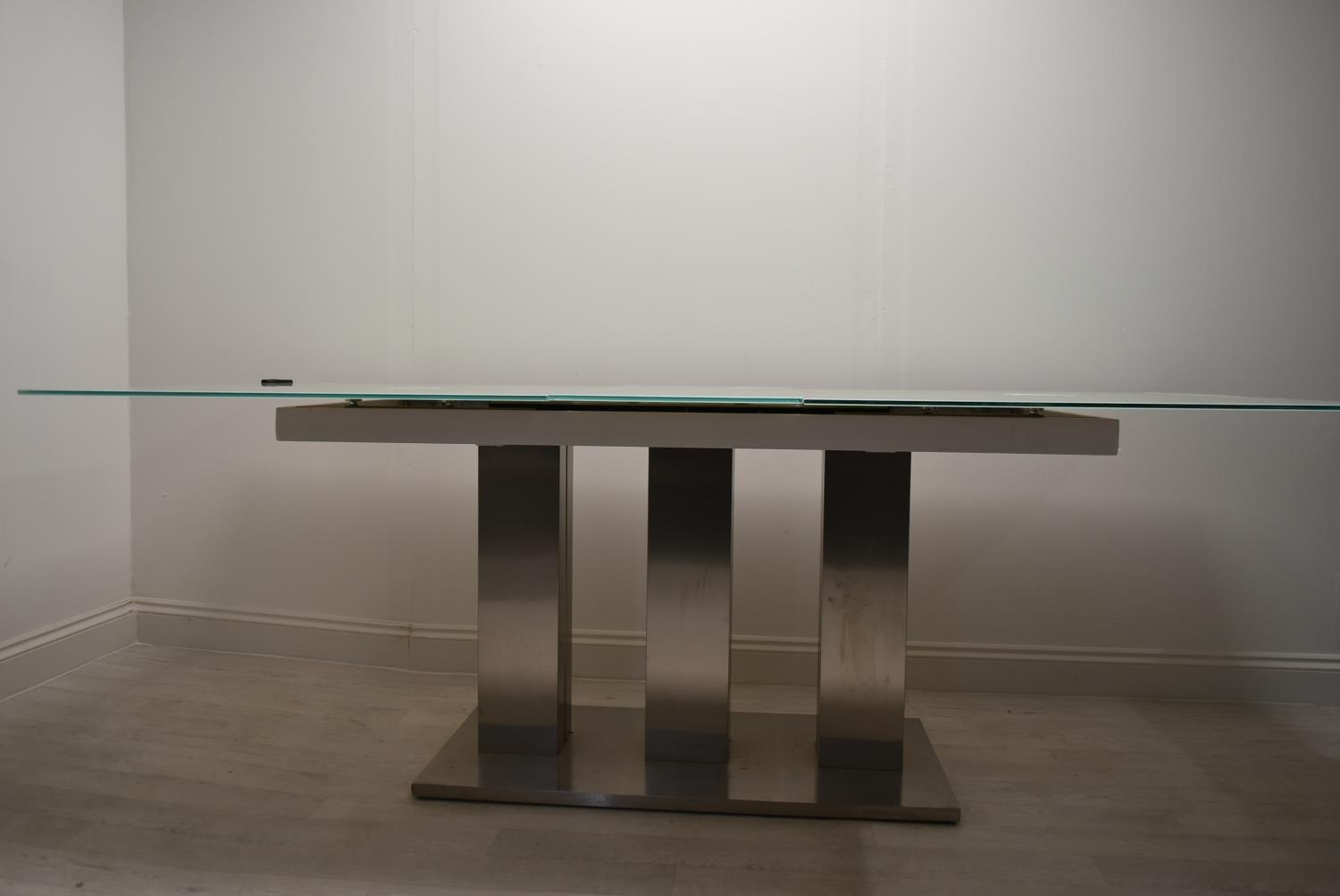 A contemporary extending glass dining table on brushed metal base. H.76 W.221 D.90cm