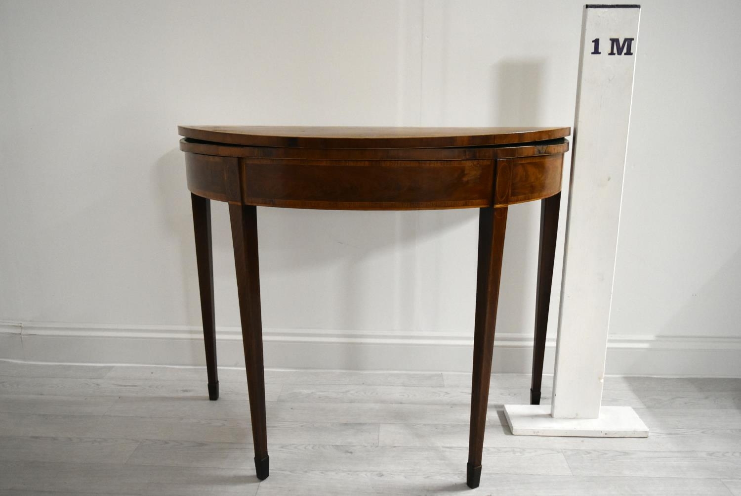 A George III cross banded mahogany fold over demi lune games table, raised on square tapering - Image 2 of 12