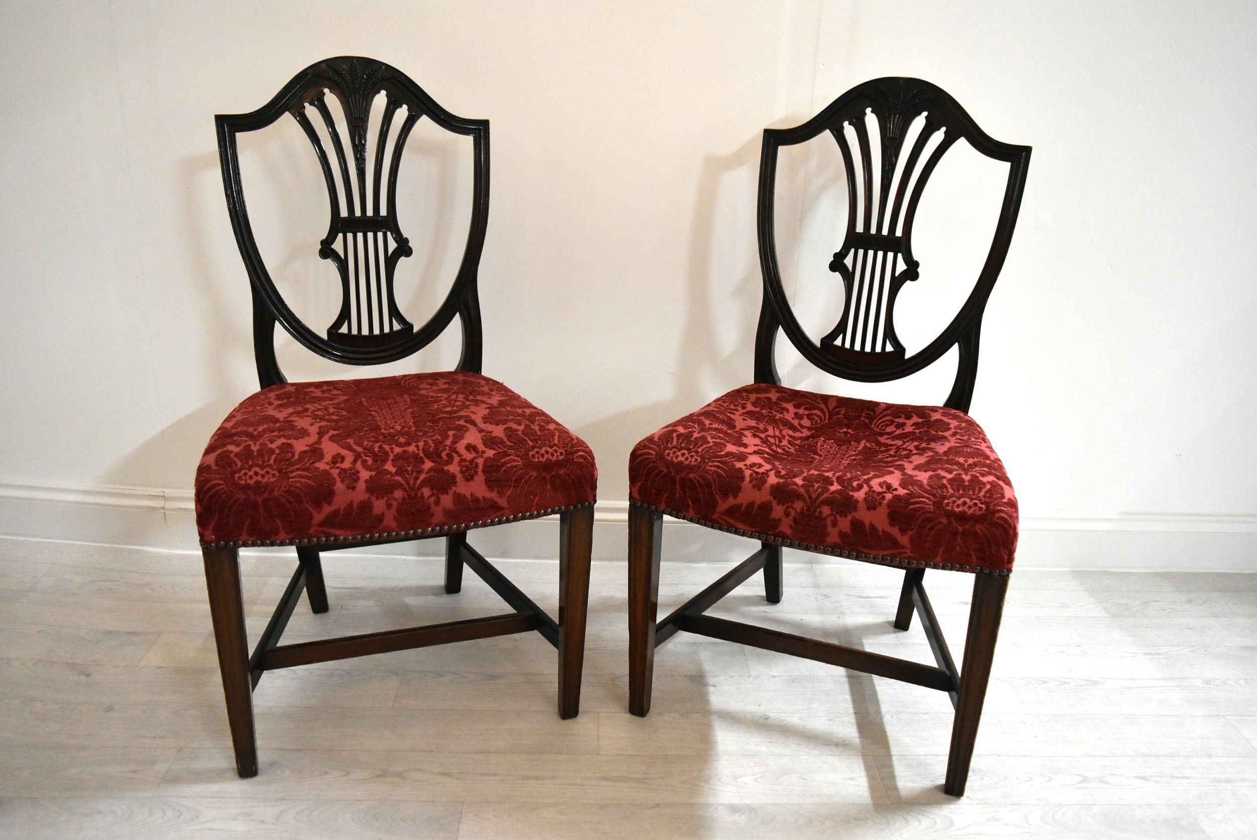 A pair of mahogany framed Hepplewhite style shield back dining chairs, each with stuff over seats.