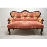 A late 19th / early 20th century mahogany framed French style settee with scroll arms raised on