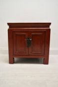 A Chinese style red painted twin door bedside cupboard opening to reveal shelves and single