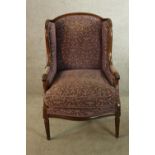 An early 20th century mahogany show framed wing back upholstered armchair raised on tapering