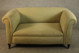 An early 20th century yellow upholstered drop end two seater sofa raised on turned supports