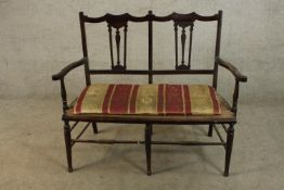 An Edwardian mahogany framed open arm two seater bench with pierced splat back raised turned