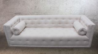 A contemporary white deep buttoned cotton upholstered sofa with cylindrical bolster cushions.