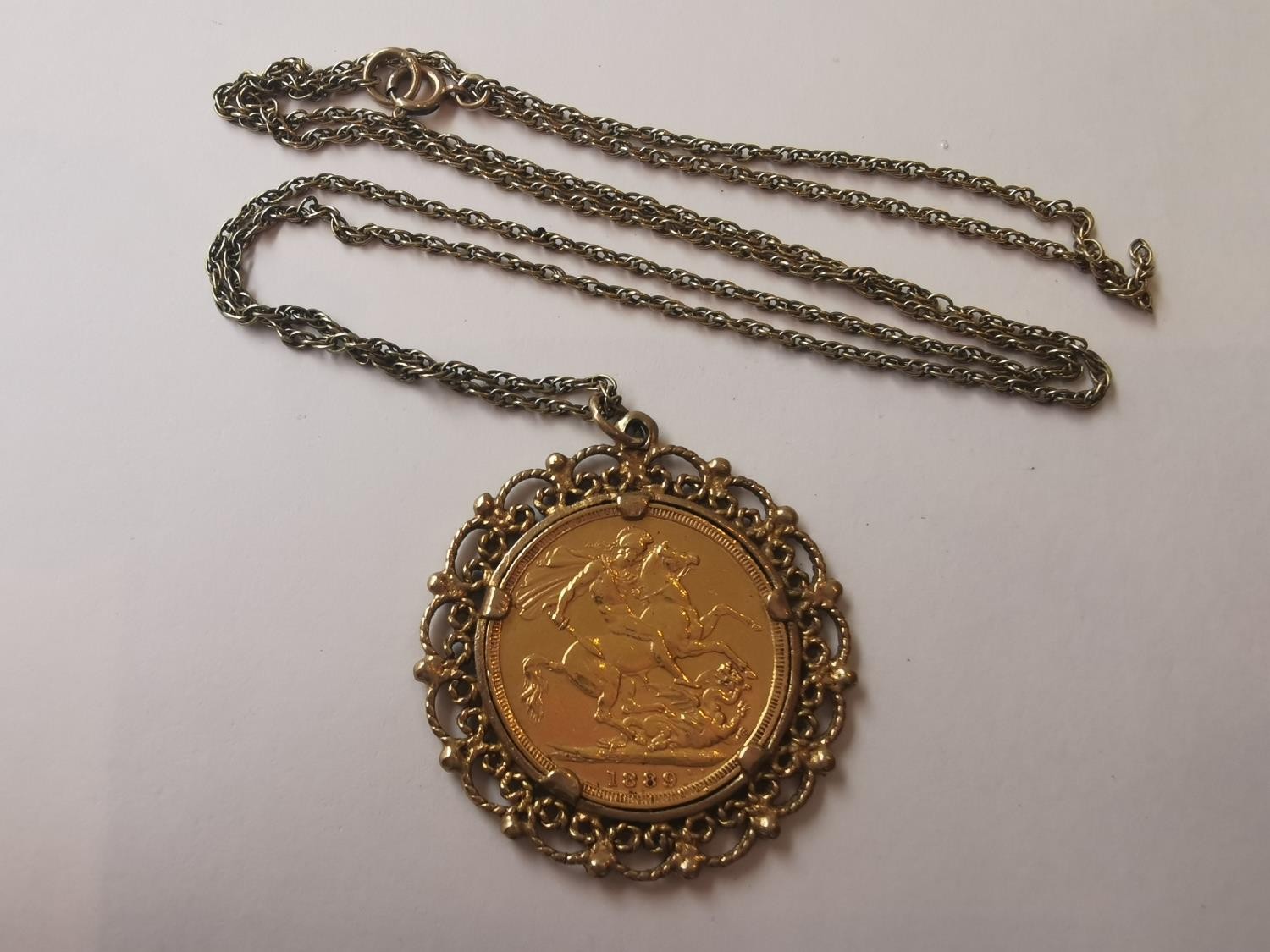 An 1889 Victorian full sovereign in filigree wirework mount on a 9 carat yellow gold rope chain. (