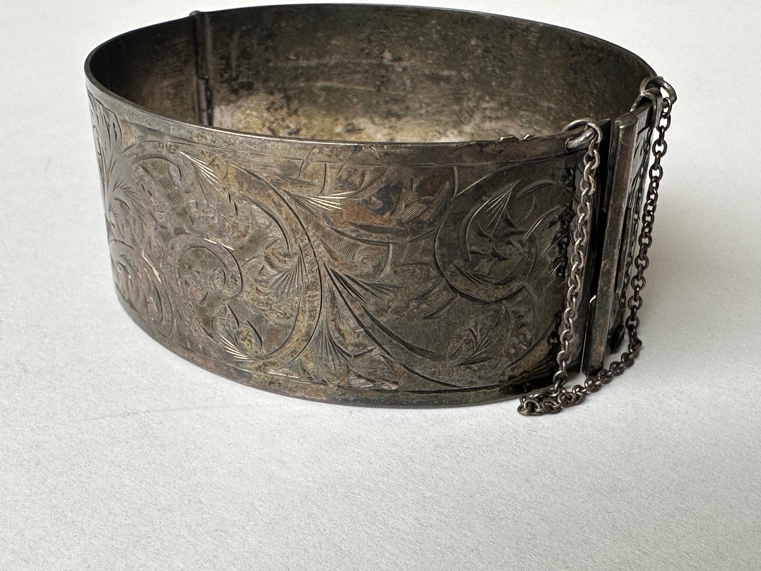 An Art Deco engraved wide silver bangle, decorated with scrolling foliate design. Fastens with a