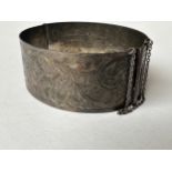 An Art Deco engraved wide silver bangle, decorated with scrolling foliate design. Fastens with a
