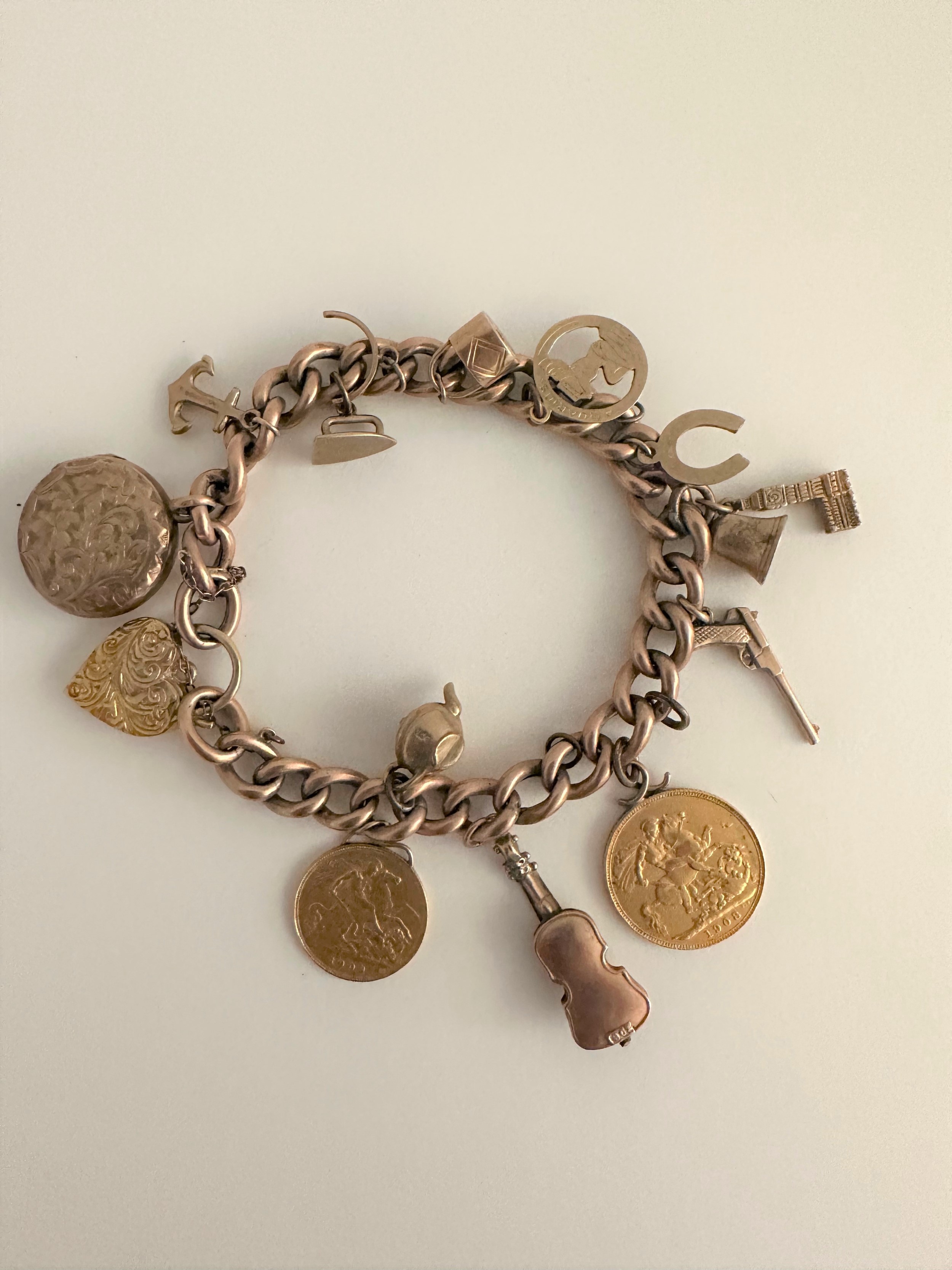 A 9 carat rose gold curb link charm bracelet with engraved heart padlock clasp. Bracelet has 13