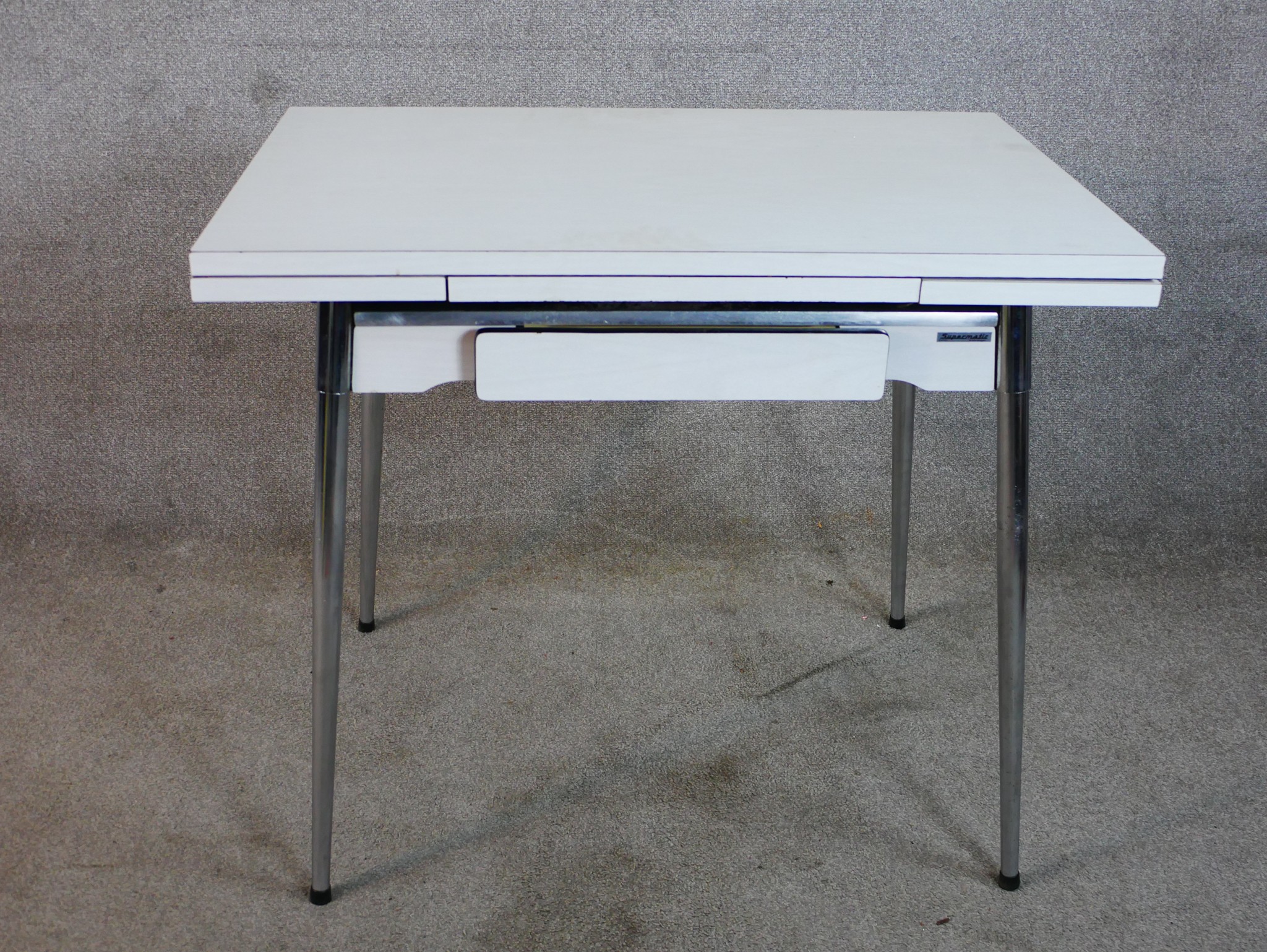 A mid 20th century Supamatic formica drawleaf dining table raised on chrome plated supports