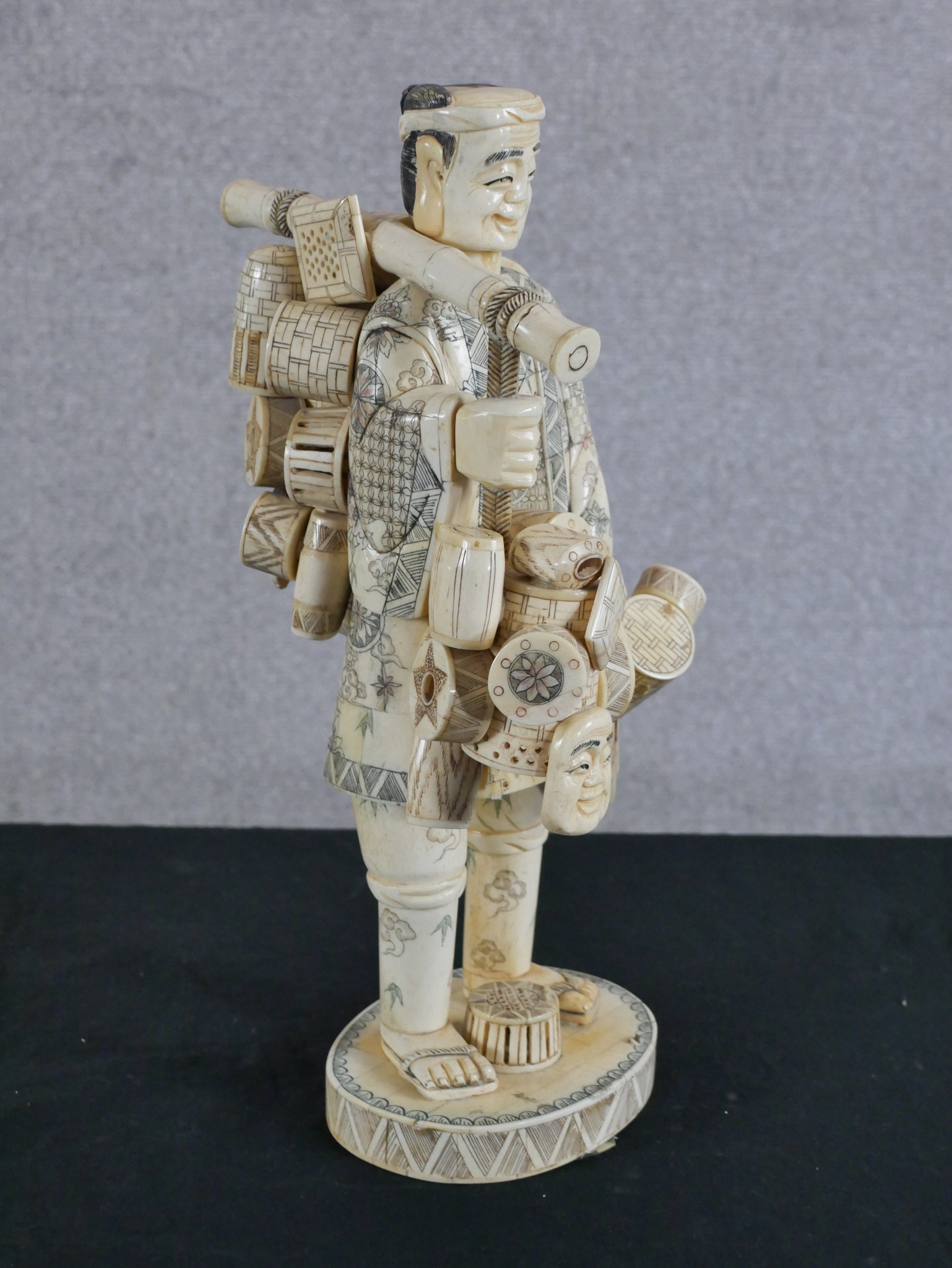 A Japanese Meiji period (1868-1912) carved bone okimono travelling salesman raised on incised oval - Image 2 of 3