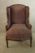 An early 20th century mahogany show framed wing back upholstered armchair raised on tapering