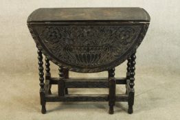 An early 20th century carved oak drop leaf gateleg table raised on barley twist supports terminating