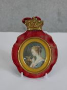 A 19th century painted miniature of a women with a yellow bird mounted in a red velvet oval frame
