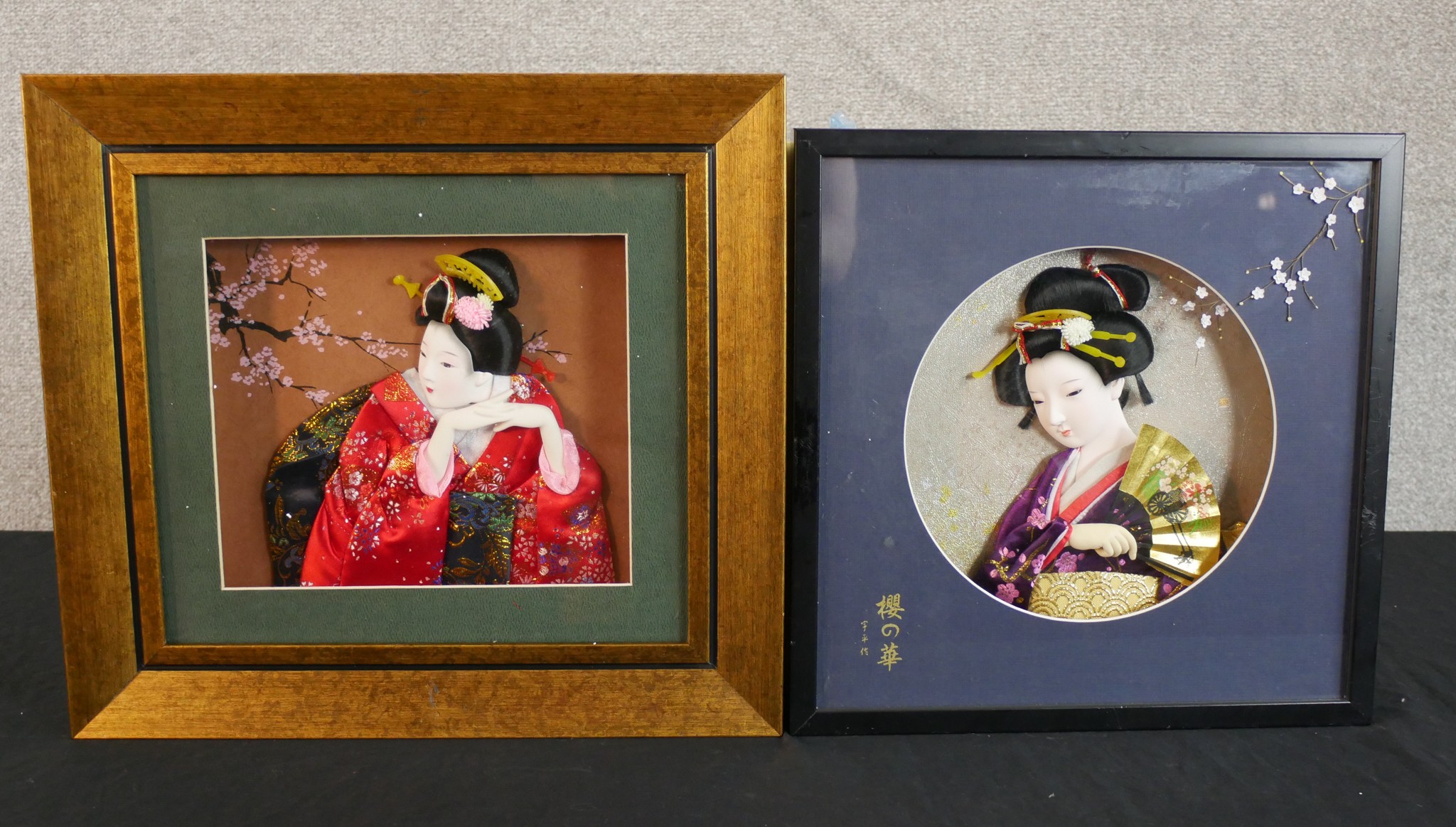 Two highly detailed Japanese geisha models in traditional dress housed in wooden frames. The largest
