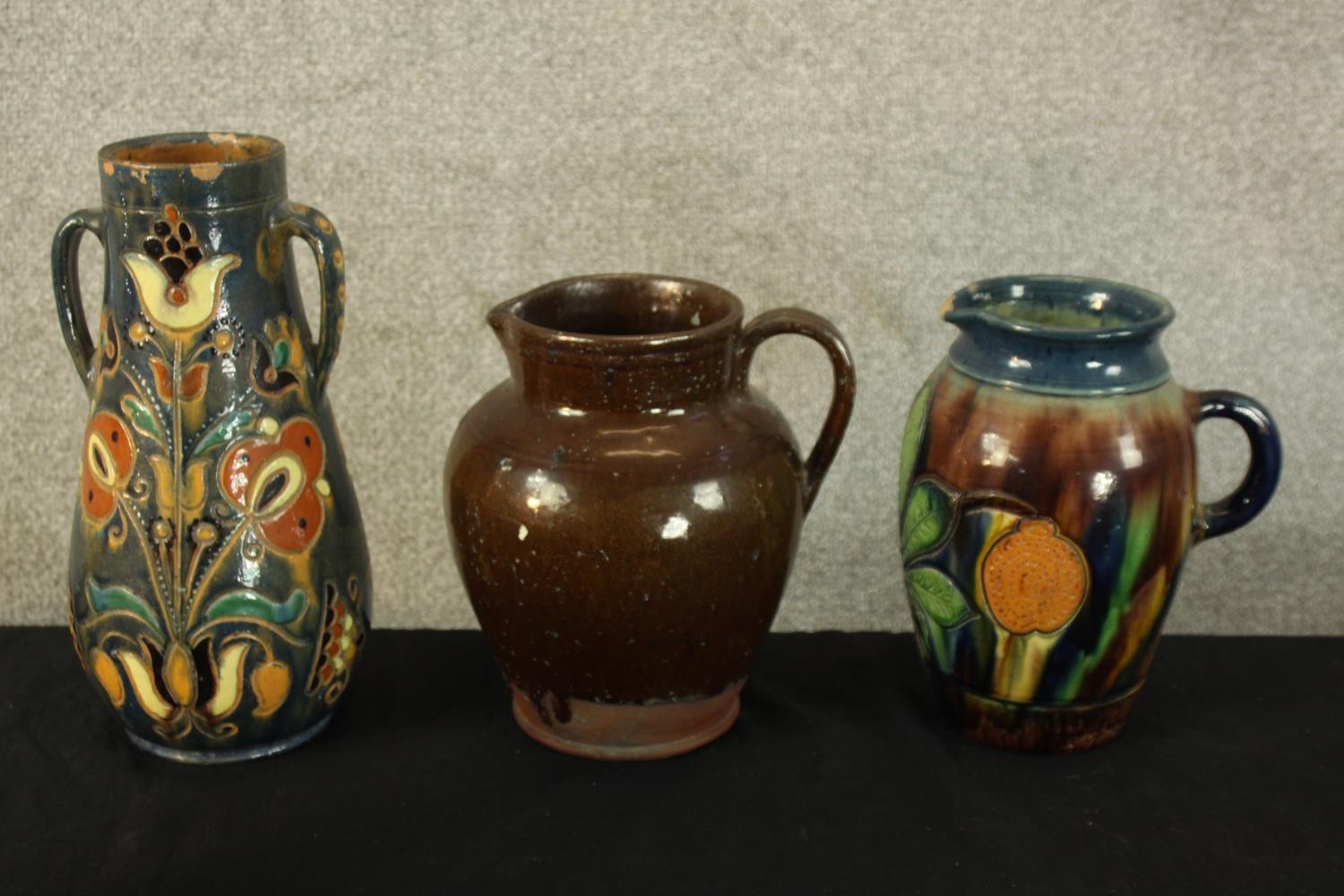 Three studio pottery jugs. Two with a floral decoration. H.30cm (largest).