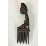A carved tribal African comb with a seated sculpted figure as the handle. H.23 x W.7cm.