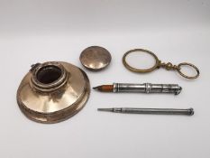 A silver hinged lidded ink well, two silver sliding miniature pencils and golf plated magnifier.