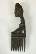 A carved tribal African comb with a seated sculpted figure as the handle. H.23 x W.7cm.