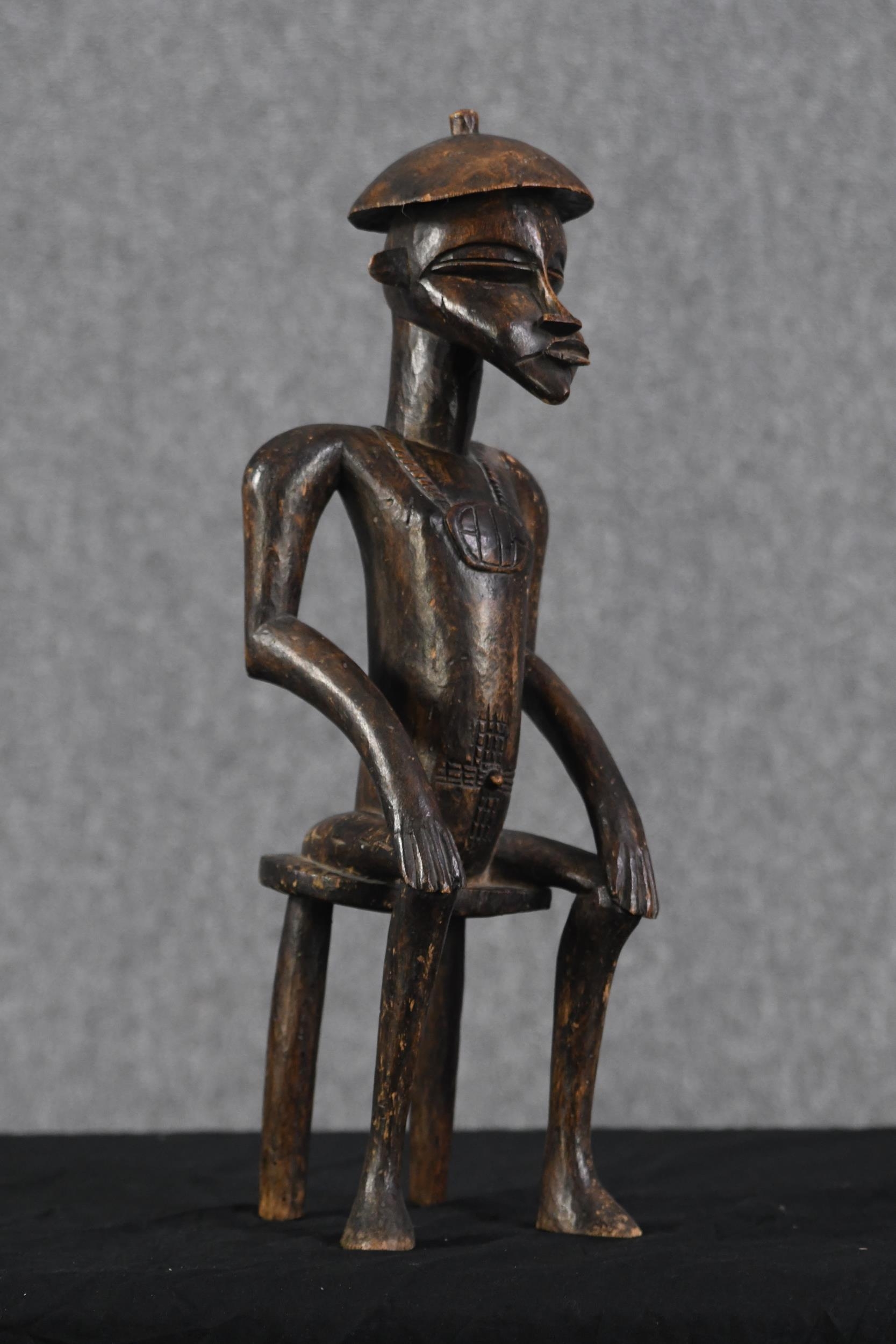 A carved hardwood figure. Tribal Art. A seated man with a decorated chest. H.53 x W.15 x D.15 cm. - Image 2 of 3