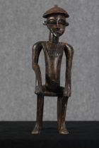 A carved hardwood figure. Tribal Art. A seated man with a decorated chest. H.53 x W.15 x D.15 cm.