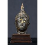 A 19th century bronze cast head of a buddha on a stepped hardwood plinth. With the remains of old