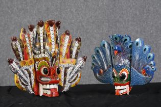 Two Sri Lankan polychrome carved wooden faces with decorative headdresses, decorated with cobras and