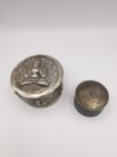 An Indian white metal (tests as silver) repousse circular box with Buddha decoration along with a