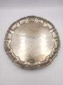 A sterling silver scalloped edge circular platter with scrolling foliate form feet. Hallmarked: JP