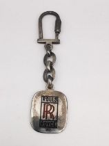 A silver and enamel Rolls Royce keychain, with red and black enamel logo and lettering. Has secure