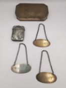 A collection of silver and white metal items, including three engraved silver drinks labels, a