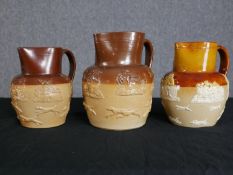 Three Doulton jugs decorated with embossed vignettes. Circa 1930. Each measure H.20 W. 19cm.