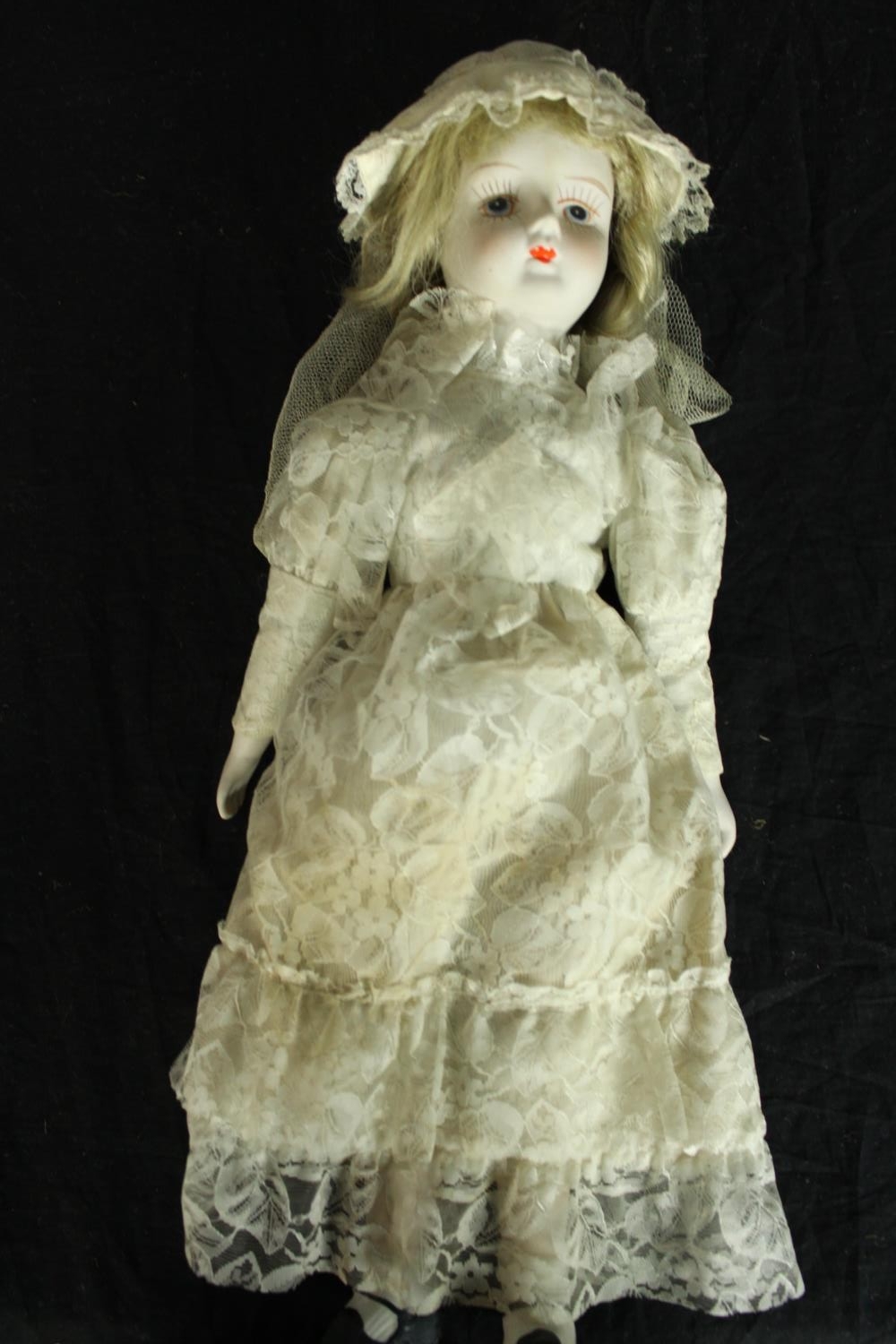 A ceramic bride doll with a hand painted face and lace clothing. Early twentieth century. H.47cm.