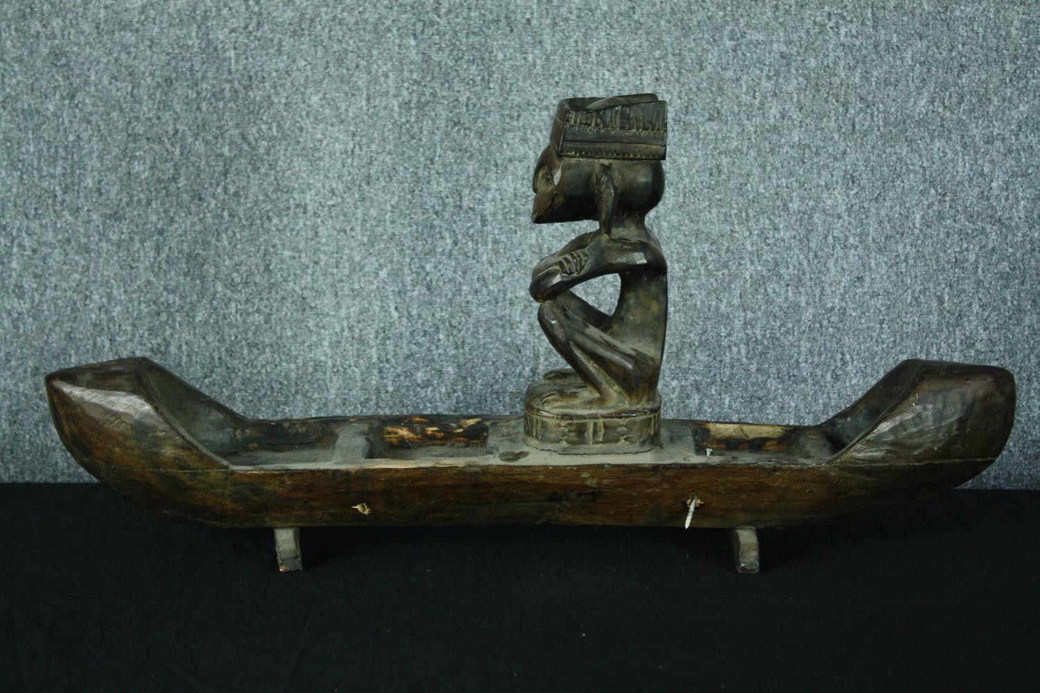 A large carved wooden canoe with a serene looking seated figure. H.39 W.80 cm.
