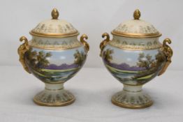 A pair of hand painted lidded twin handled ceramic urns with lake scene with swans and gilded